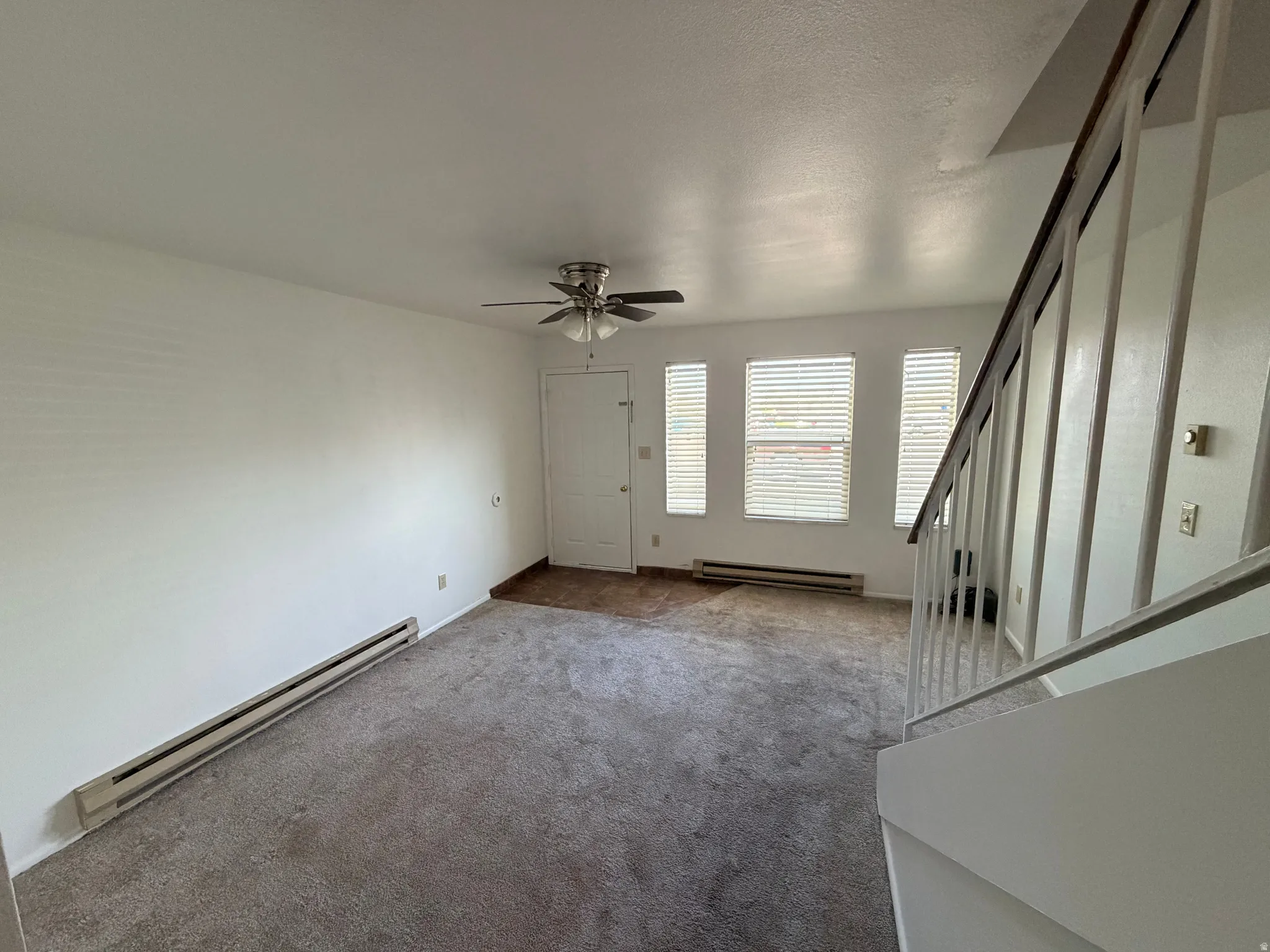 Unfurnished living room featuring baseboard heating, carpet floors, and a ceiling fan