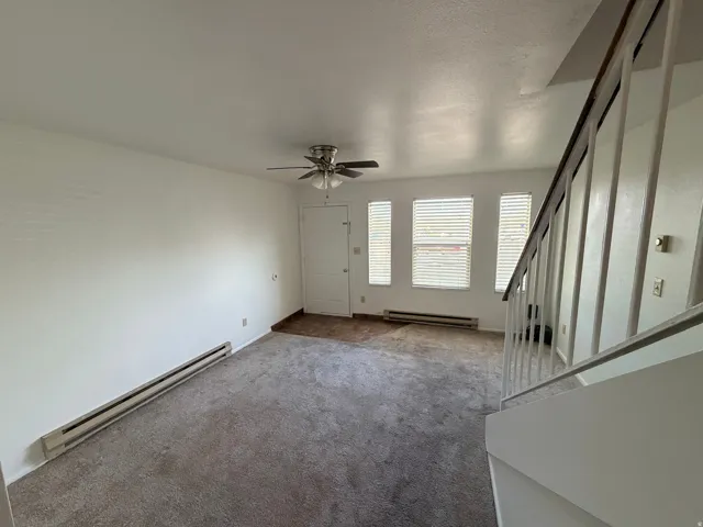 Unfurnished living room featuring baseboard heating, carpet floors, and a ceiling fan