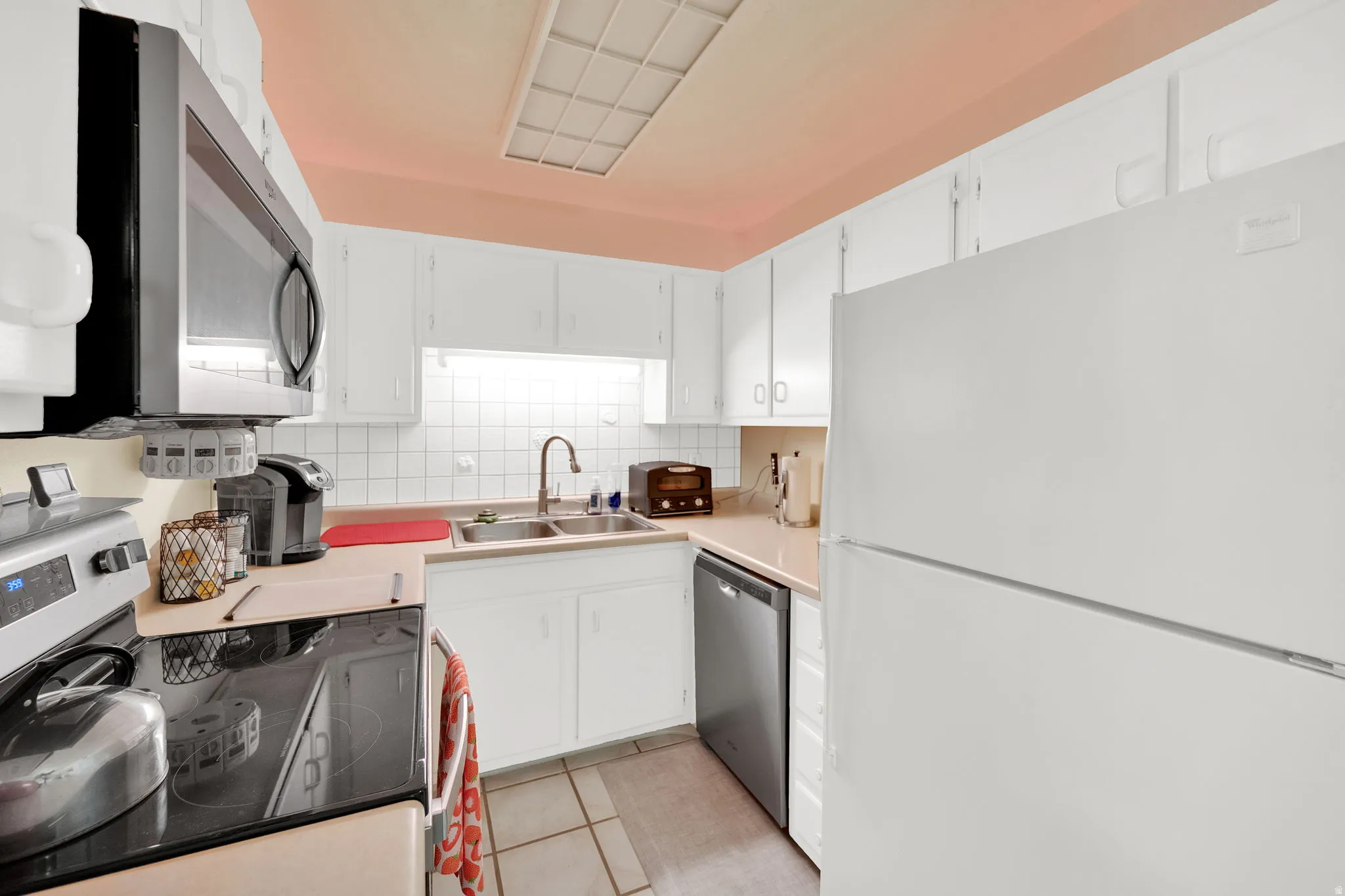 Kitchen with stainless steel appliances, white cabinetry, light tile patterned flooring, light countertops, and backsplash