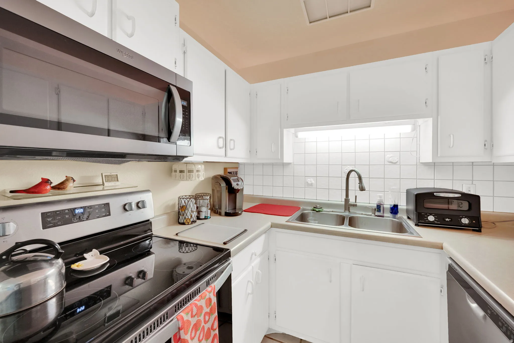 Kitchen with stainless steel appliances, white cabinetry, light countertops, and decorative backsplash
