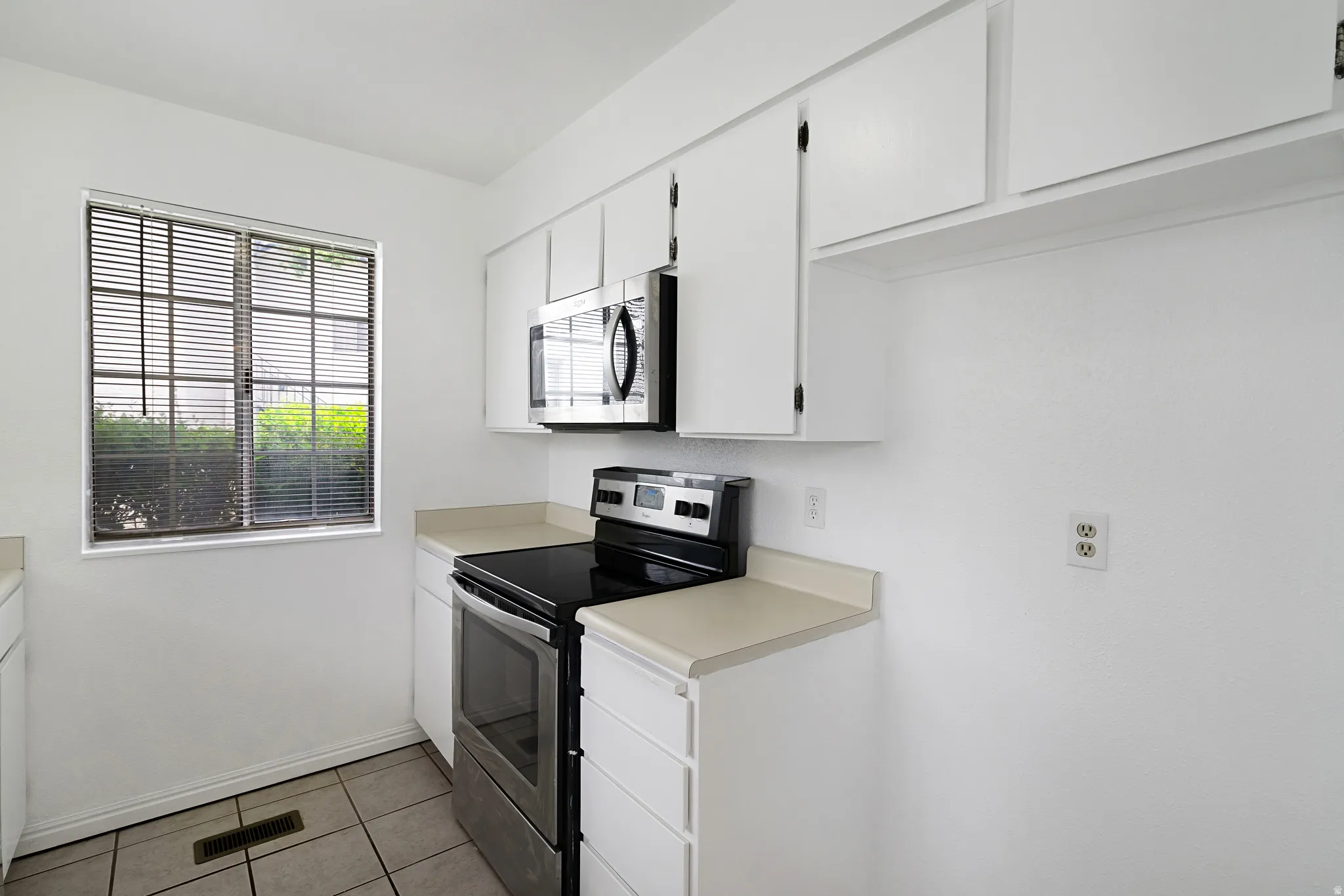 Kitchen with stainless steel appliances, white cabinets, light countertops, and light tile patterned floors