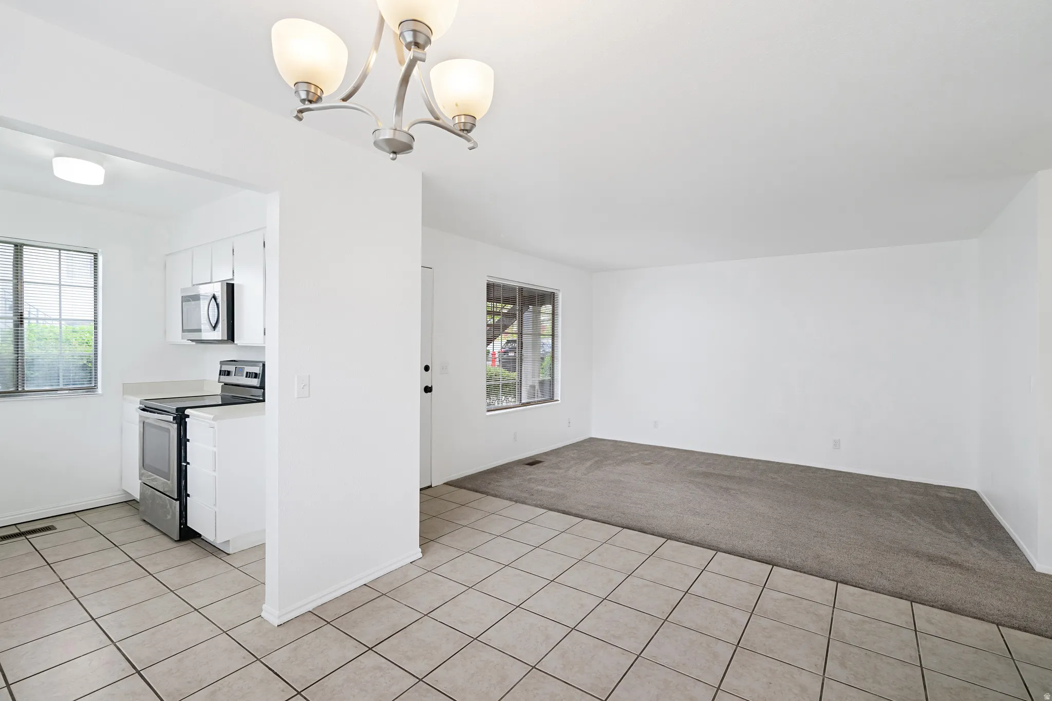 Kitchen featuring stainless steel appliances, light carpet, white cabinets, light countertops, and light tile patterned floors