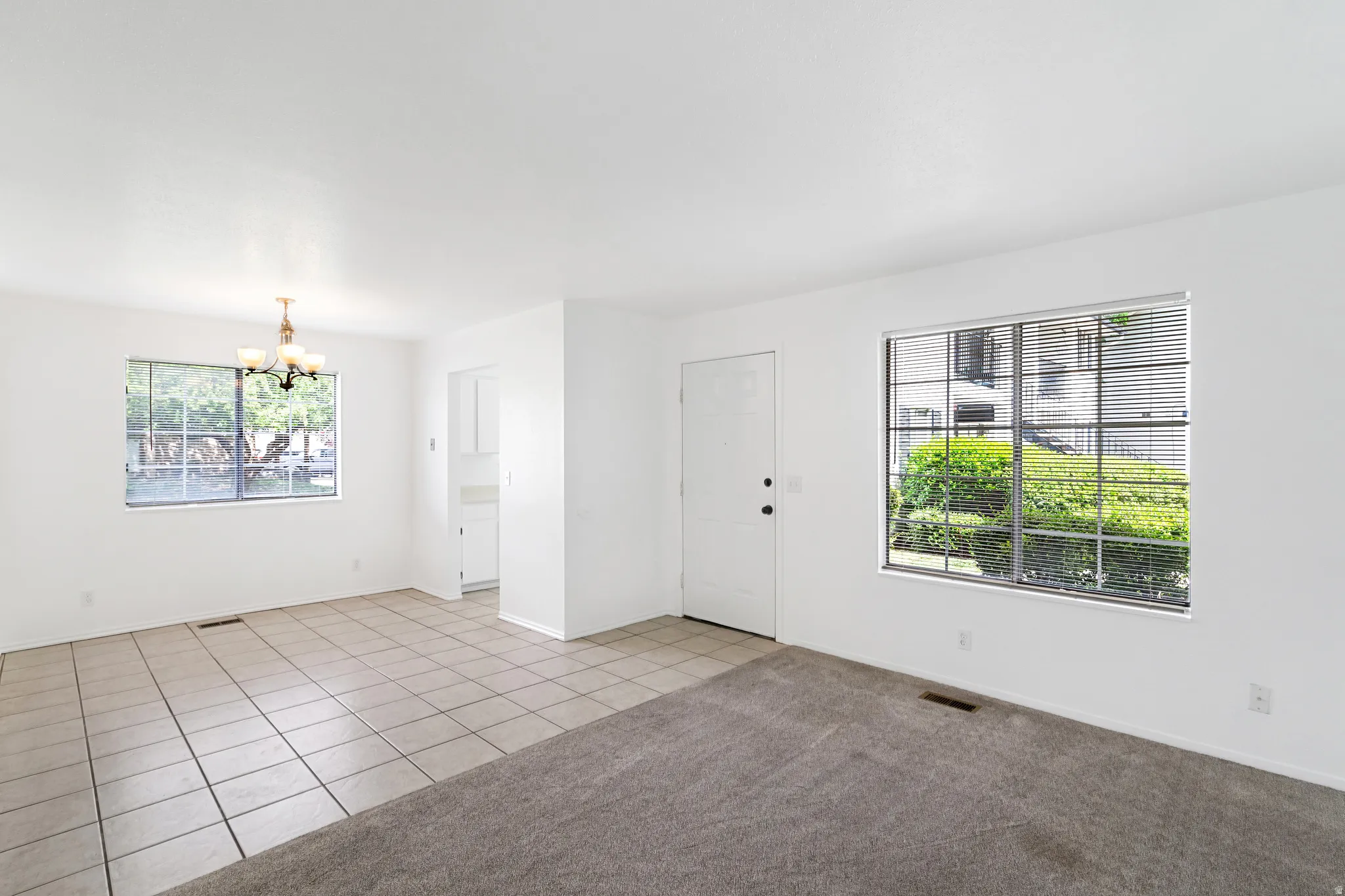 Living room featuring suspended lighting, light tile patterned flooring, and light carpet