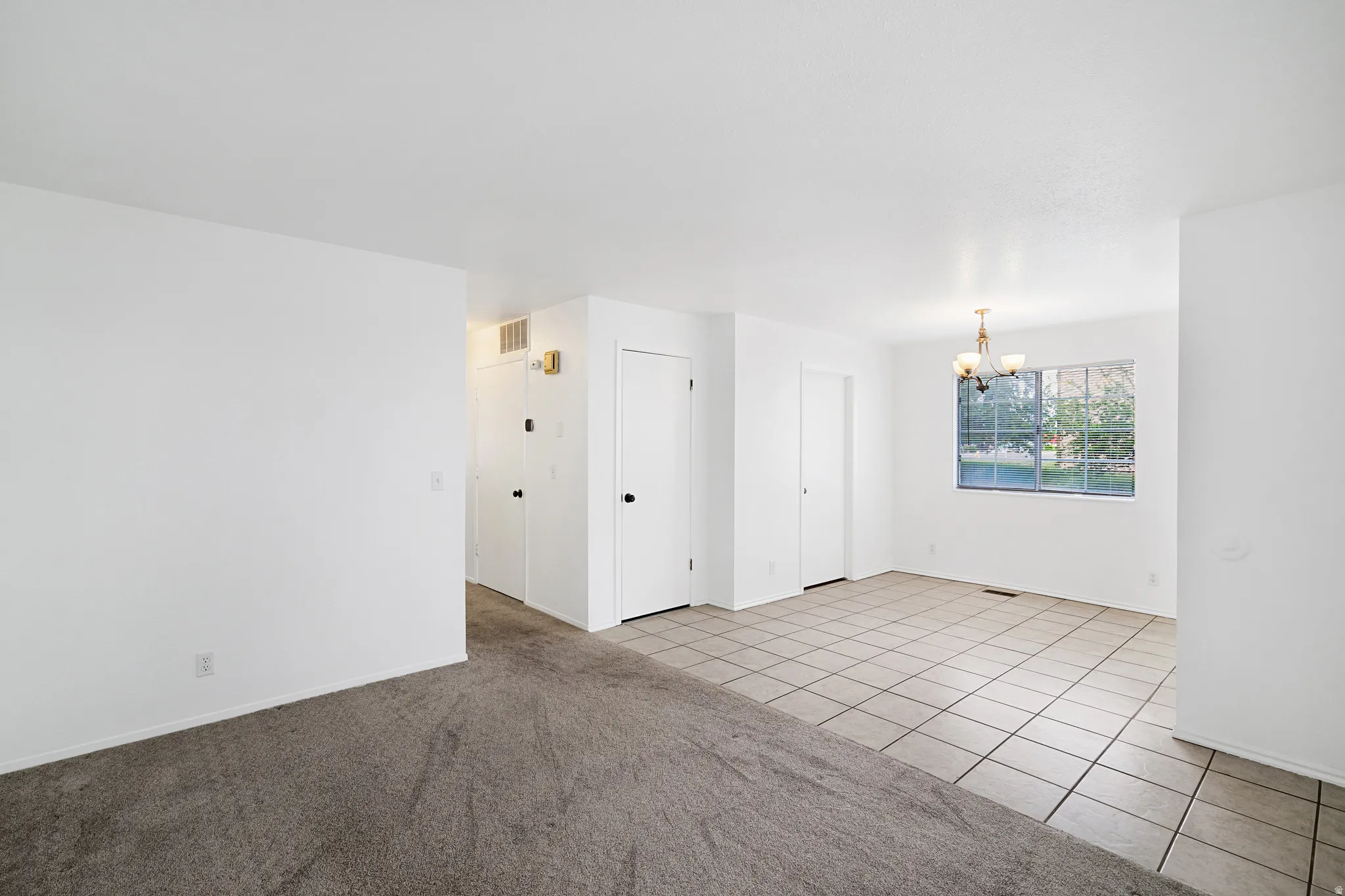 Living room  & dining area featuring suspended lighting, light tile patterned floors, and light carpet