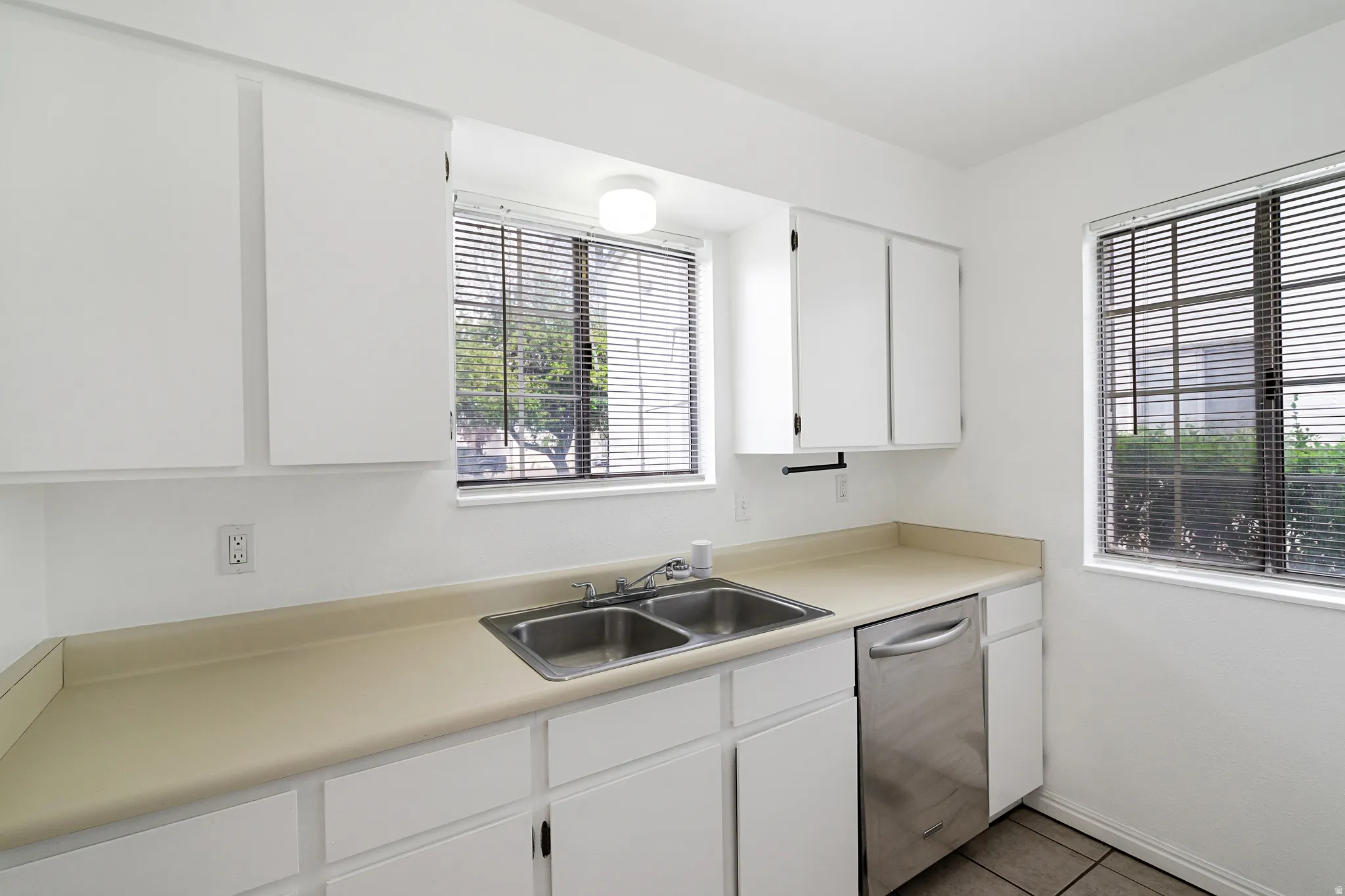 Kitchen featuring white cabinetry, stainless steel dishwasher, light countertops, and light tile patterned flooring