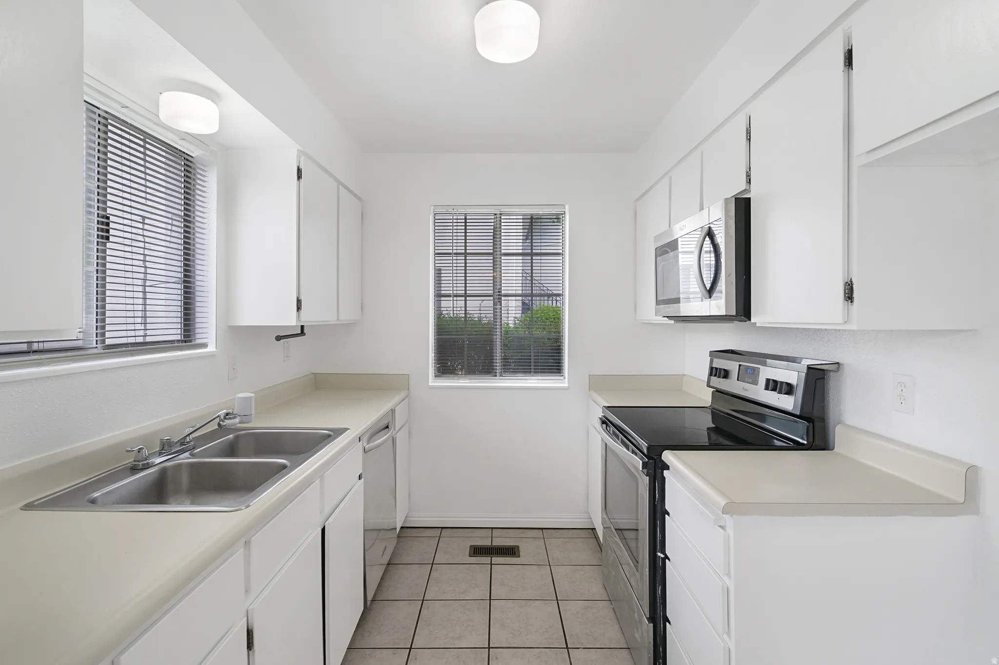 Kitchen with stainless steel appliances, white cabinetry, light countertops, and healthy amount of natural light
