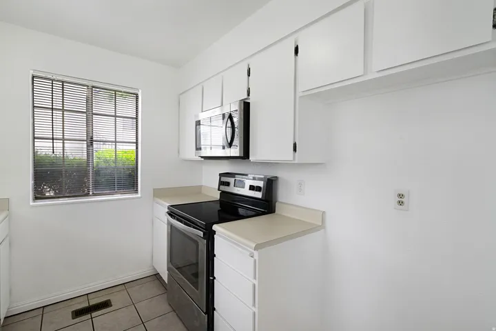 Kitchen with stainless steel appliances, white cabinets, light countertops, and light tile patterned floors