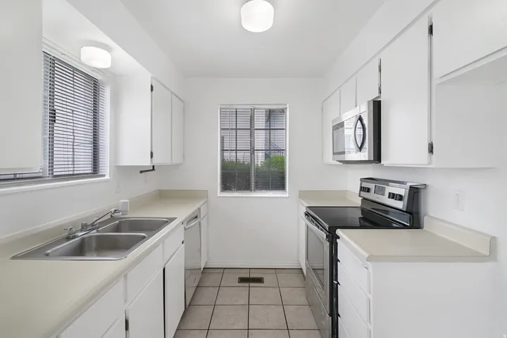 Kitchen with stainless steel appliances, white cabinetry, light countertops, and healthy amount of natural light