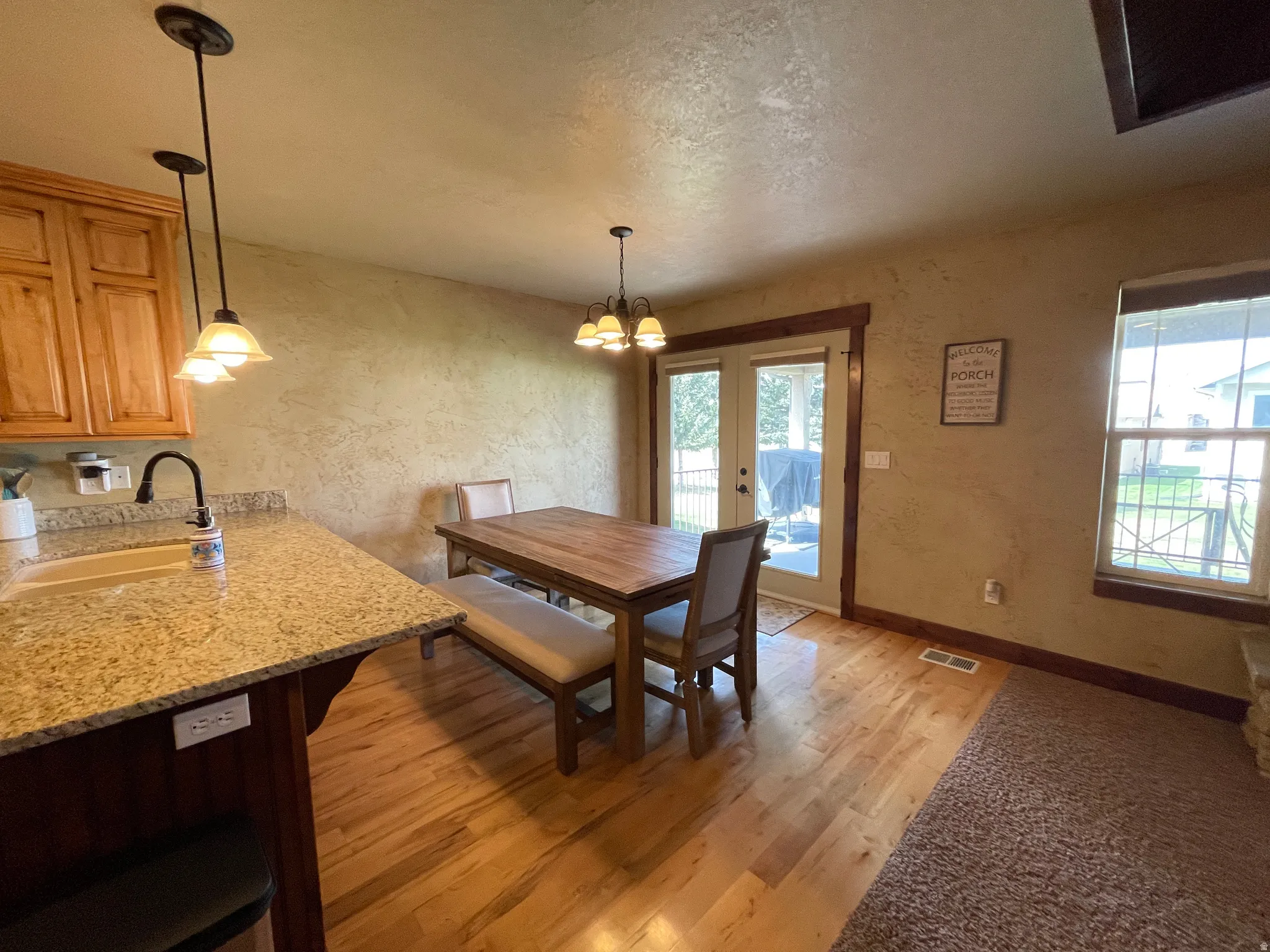 Dining room with a textured wall, light wood-type flooring, a chandelier, and a textured ceiling