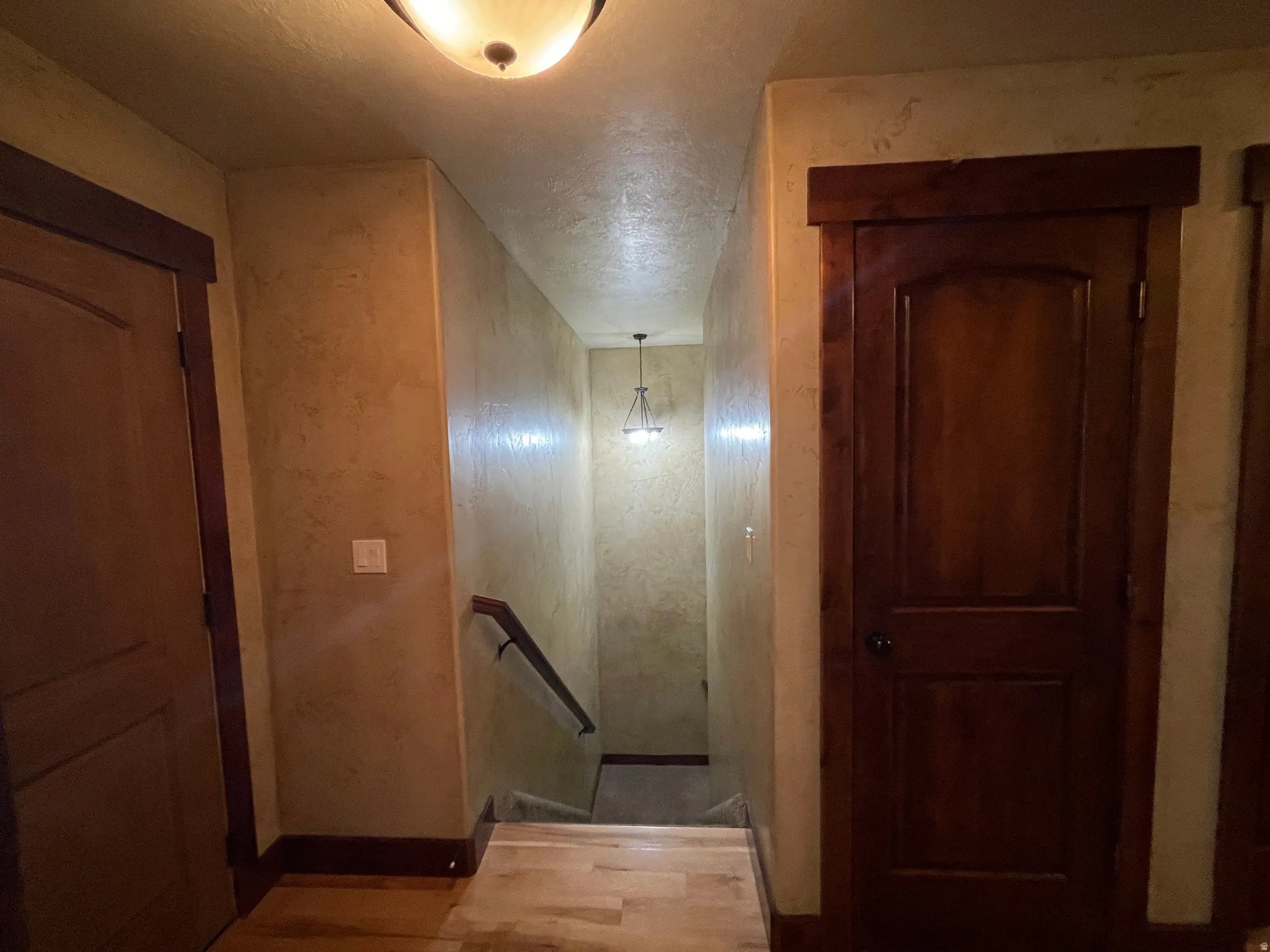 Hall with an upstairs landing, light wood finished floors, and a textured ceiling