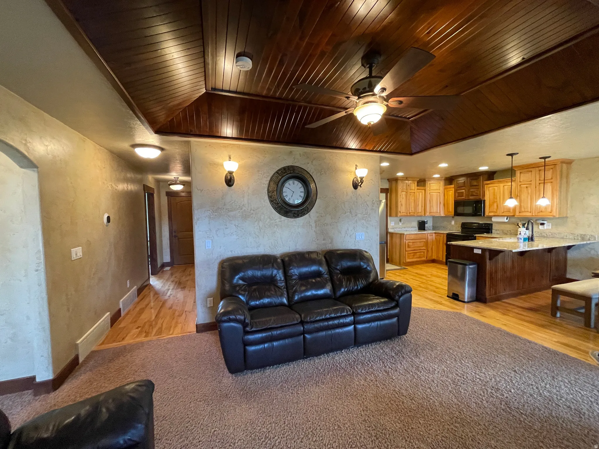Living room with a textured wall, a vaulted wood ceiling, a ceiling fan, light carpet, and arched walkways
