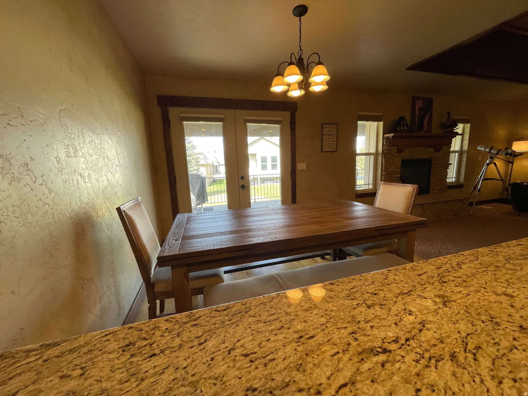 Dining room featuring hanging lights, french doors, a fireplace with raised hearth, and a textured wall