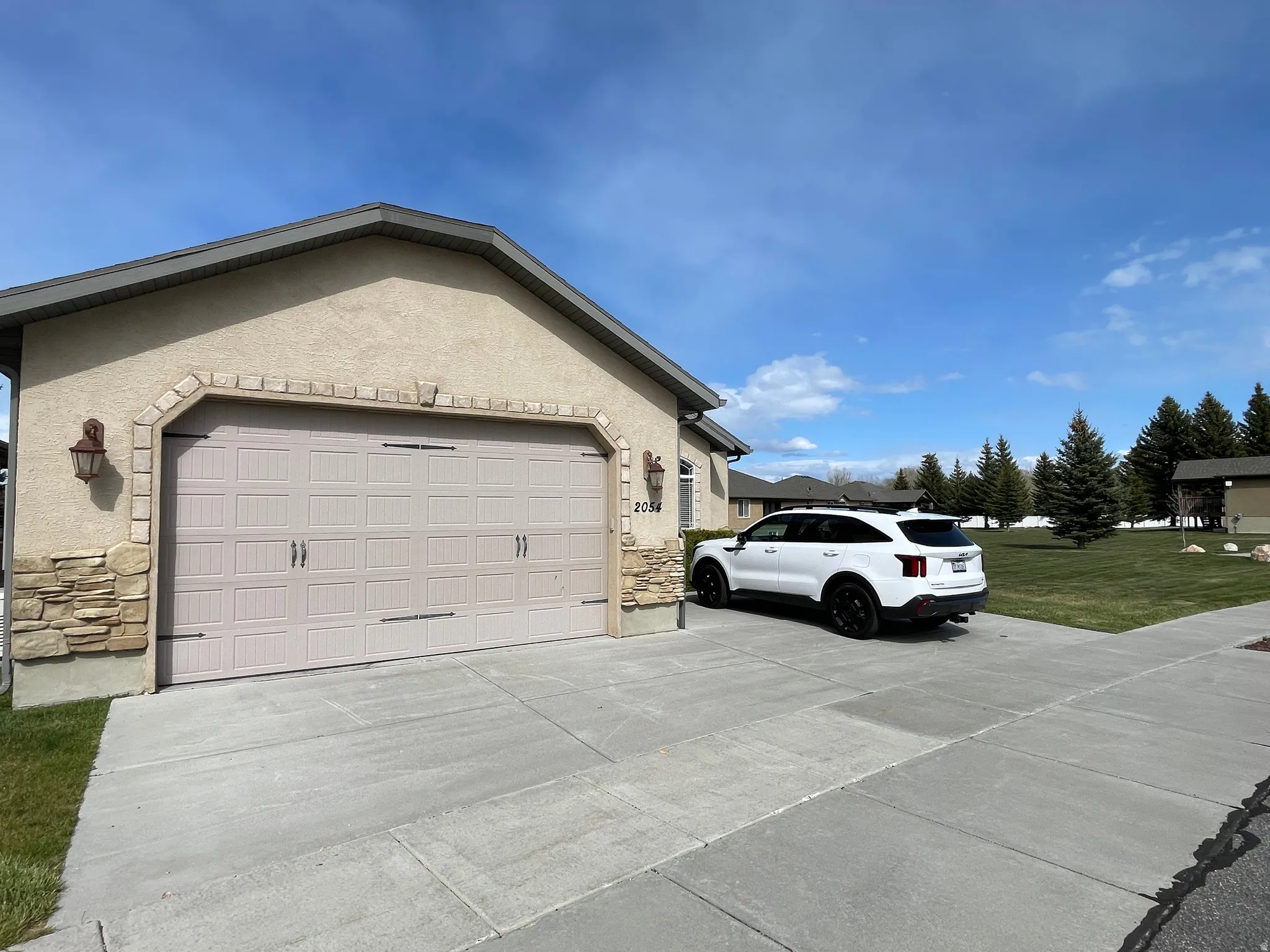 View of home's exterior with stone siding, driveway, stucco siding, an attached garage, and a lawn