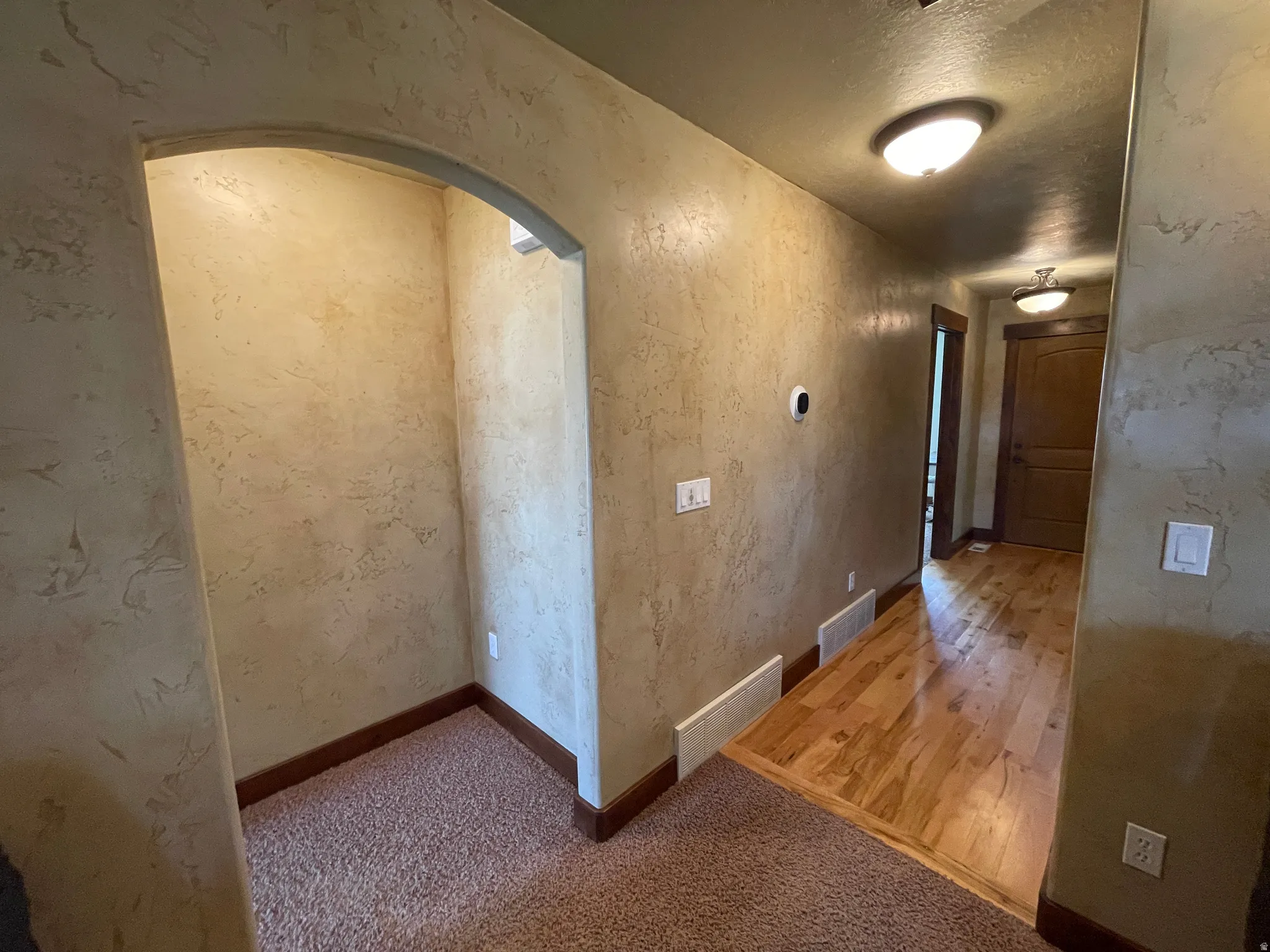 Hallway featuring a textured wall, arched walkways, a textured ceiling, and light carpet