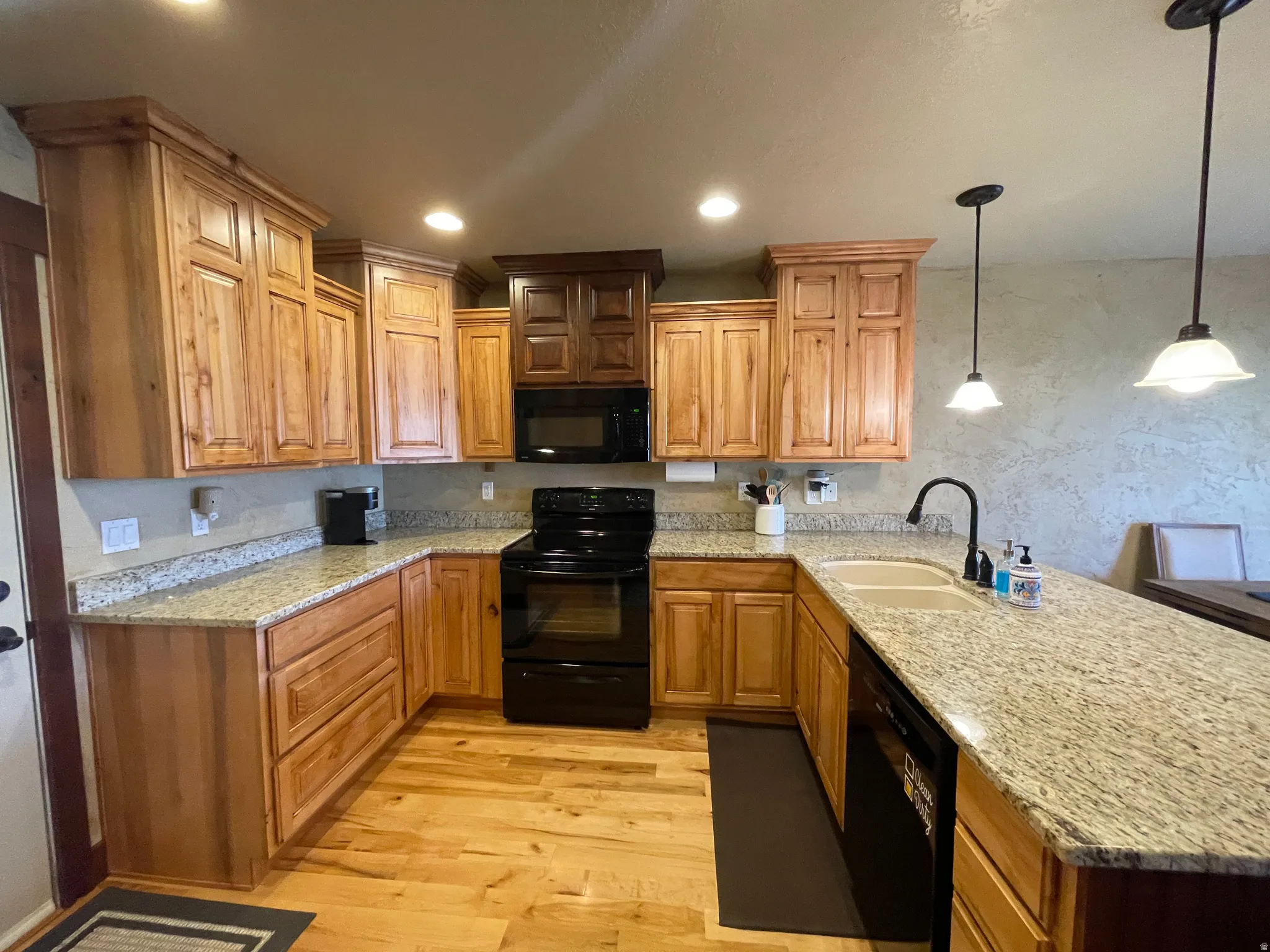 Kitchen featuring a peninsula, black appliances, light stone countertops, light wood finished floors, and decorative light fixtures