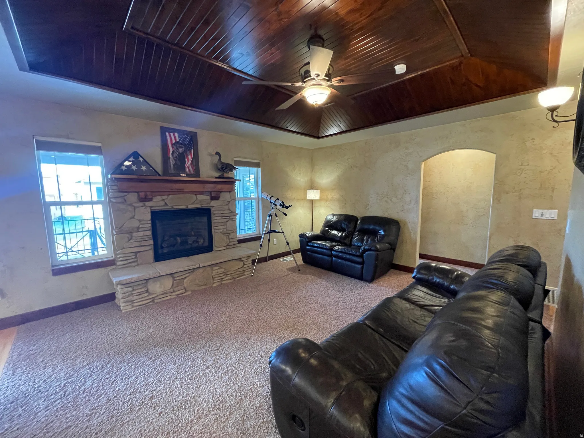 Living area featuring a wooden tray ceiling, a ceiling fan, carpet, arched walkways, and a fireplace