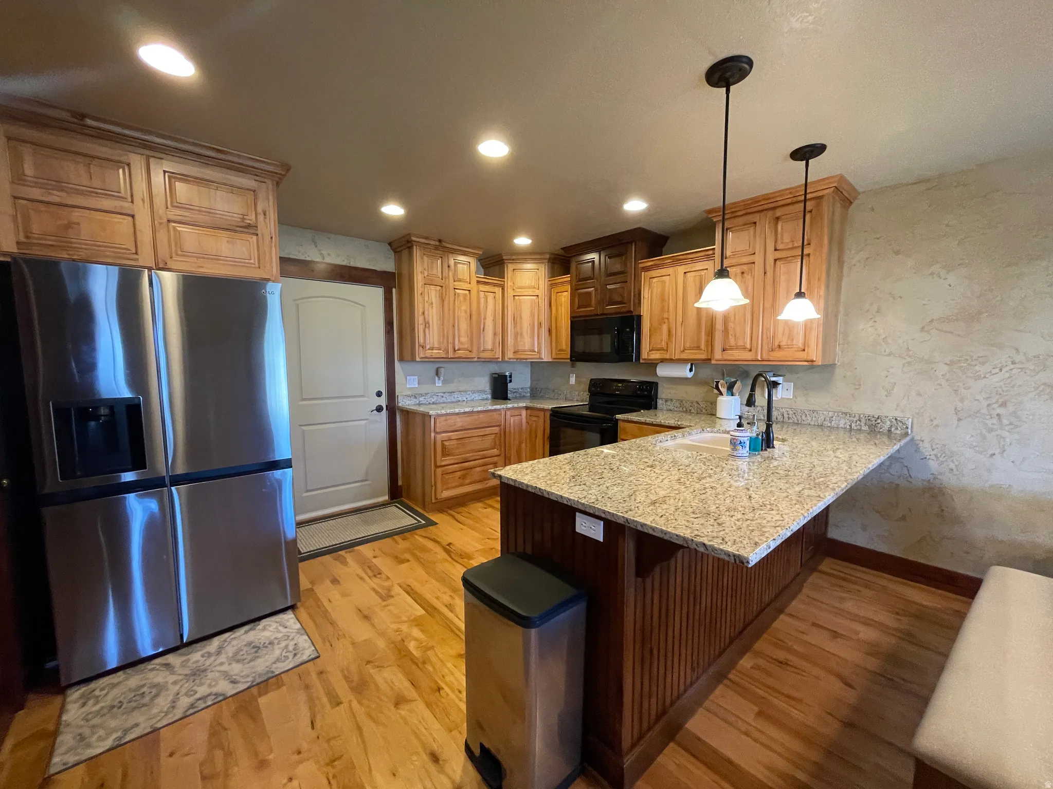 Kitchen with black appliances, a peninsula, a breakfast bar area, light stone counters, and pendant lighting