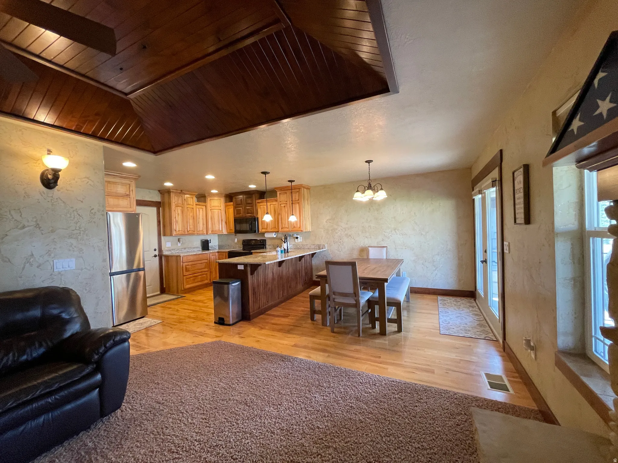 Kitchen with a kitchen bar, suspended lighting, light wood-type flooring, black appliances, and a textured wall