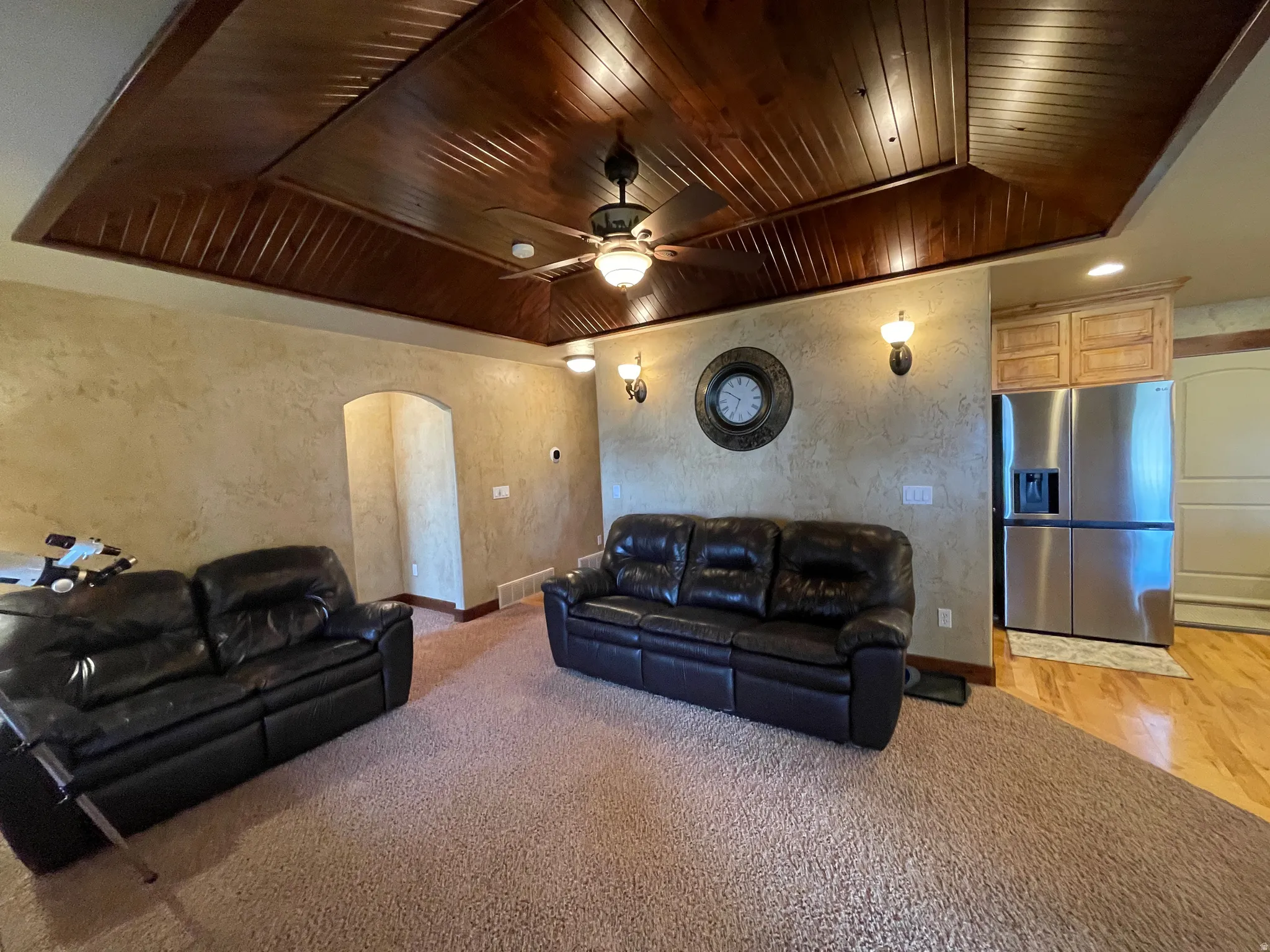 Living room with arched walkways, a textured wall, ceiling fan, light colored carpet, and wood ceiling
