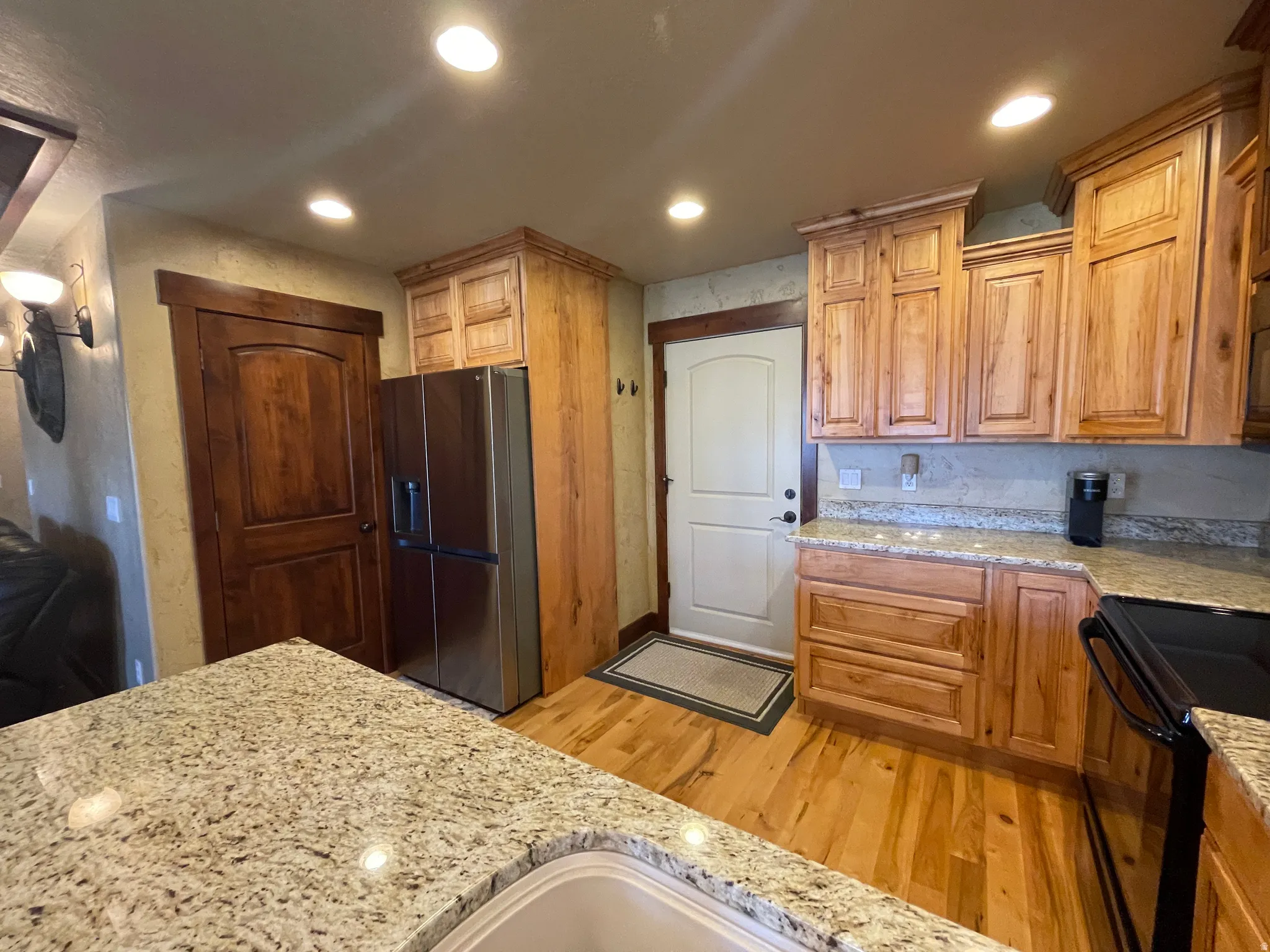 Kitchen with refrigerator with ice dispenser, light stone counters, light wood finished floors, black range with electric cooktop, and recessed lighting