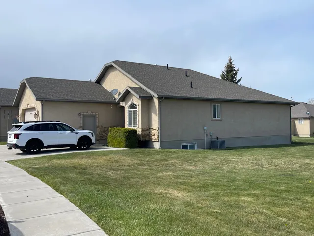 View of side of home with stucco siding, a yard, and a shingled roof