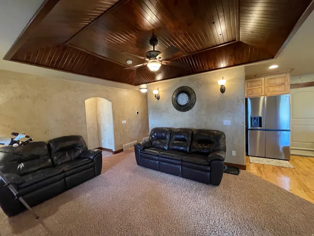 Living room with arched walkways, a textured wall, ceiling fan, light colored carpet, and wood ceiling