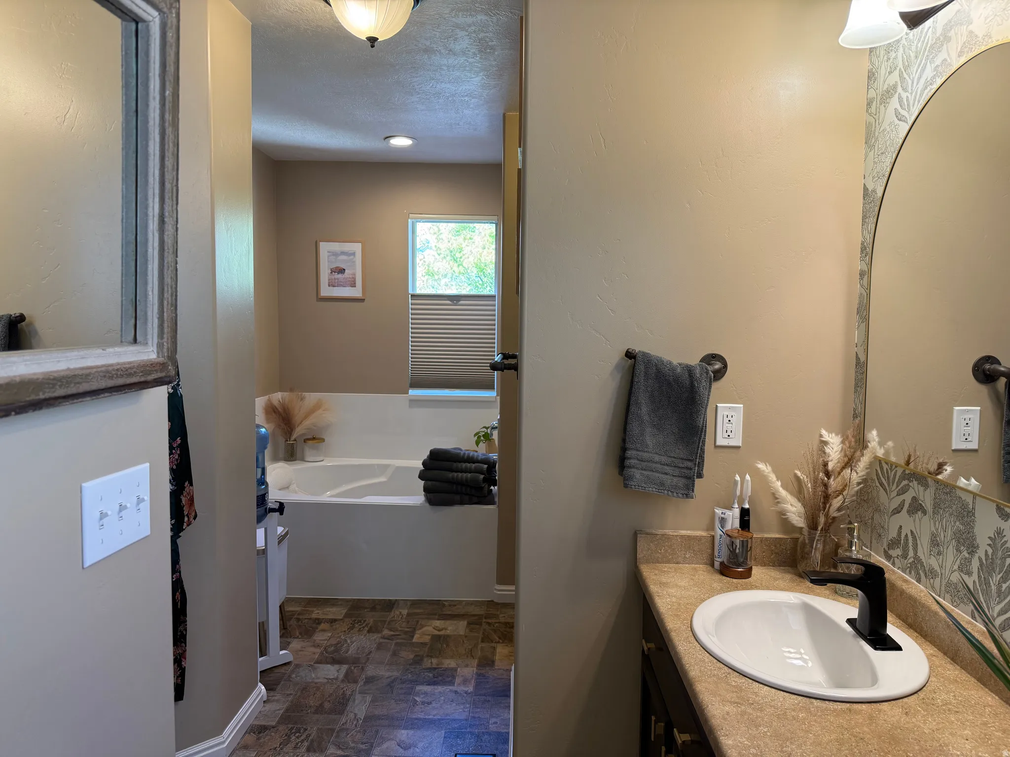 Bathroom with vanity, a bath, stone finish flooring, and a textured ceiling