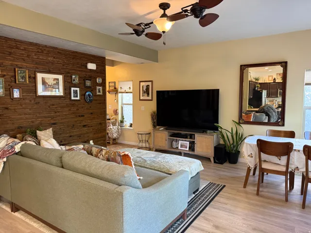Living area featuring wood walls, ceiling fan, light wood-style floors, and an accent wall