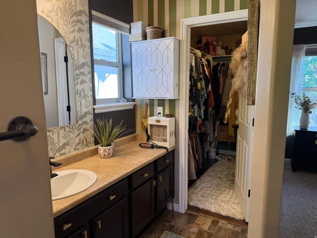 Full bathroom featuring wallpapered walls, vanity, a walk in closet, and dark flooring