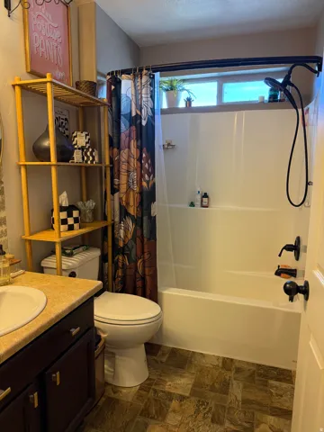 Full bathroom featuring stone finish flooring, vanity, shower / tub combo with curtain, and a textured ceiling