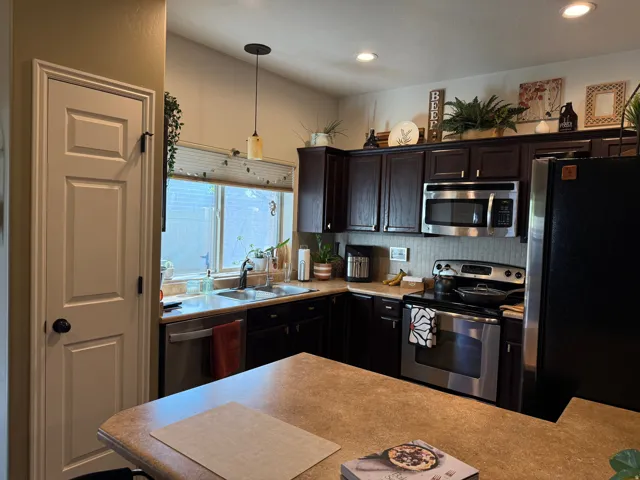 Kitchen featuring stainless steel appliances, light countertops, dark wood finish cabinetry, pendant lighting, and decorative backsplash