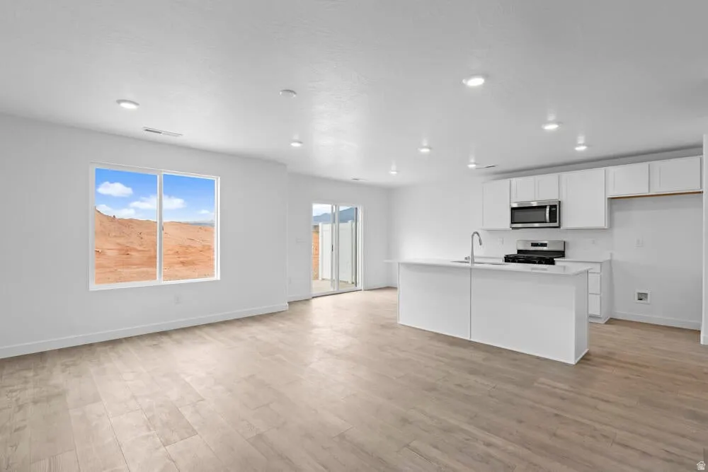 Kitchen featuring white cabinetry, a kitchen island with sink, light wood-style floors, stainless steel appliances, and open floor plan