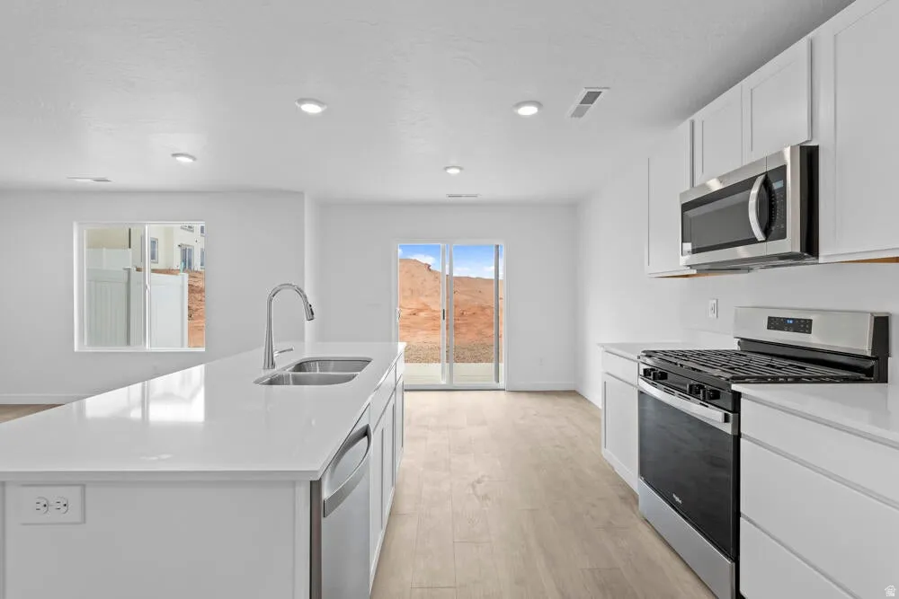 Kitchen with stainless steel appliances, an island with sink, white cabinets, light wood-type flooring, and light stone counters