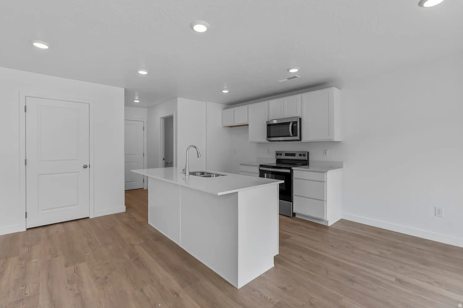 Kitchen with stainless steel appliances, white cabinetry, an island with sink, light wood-style floors, and recessed lighting