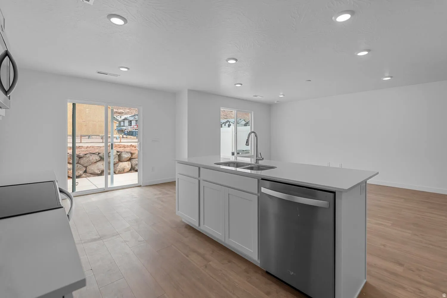 Kitchen featuring stainless steel appliances, light wood-style floors, an island with sink, white cabinets, and recessed lighting