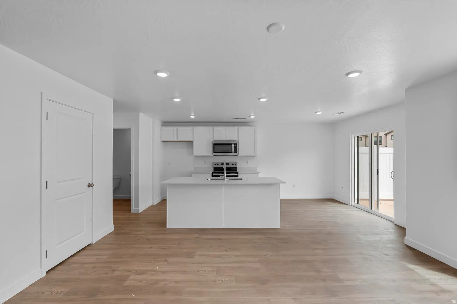 Kitchen with light wood finished floors, a kitchen island with sink, white cabinets, recessed lighting, and stainless steel appliances
