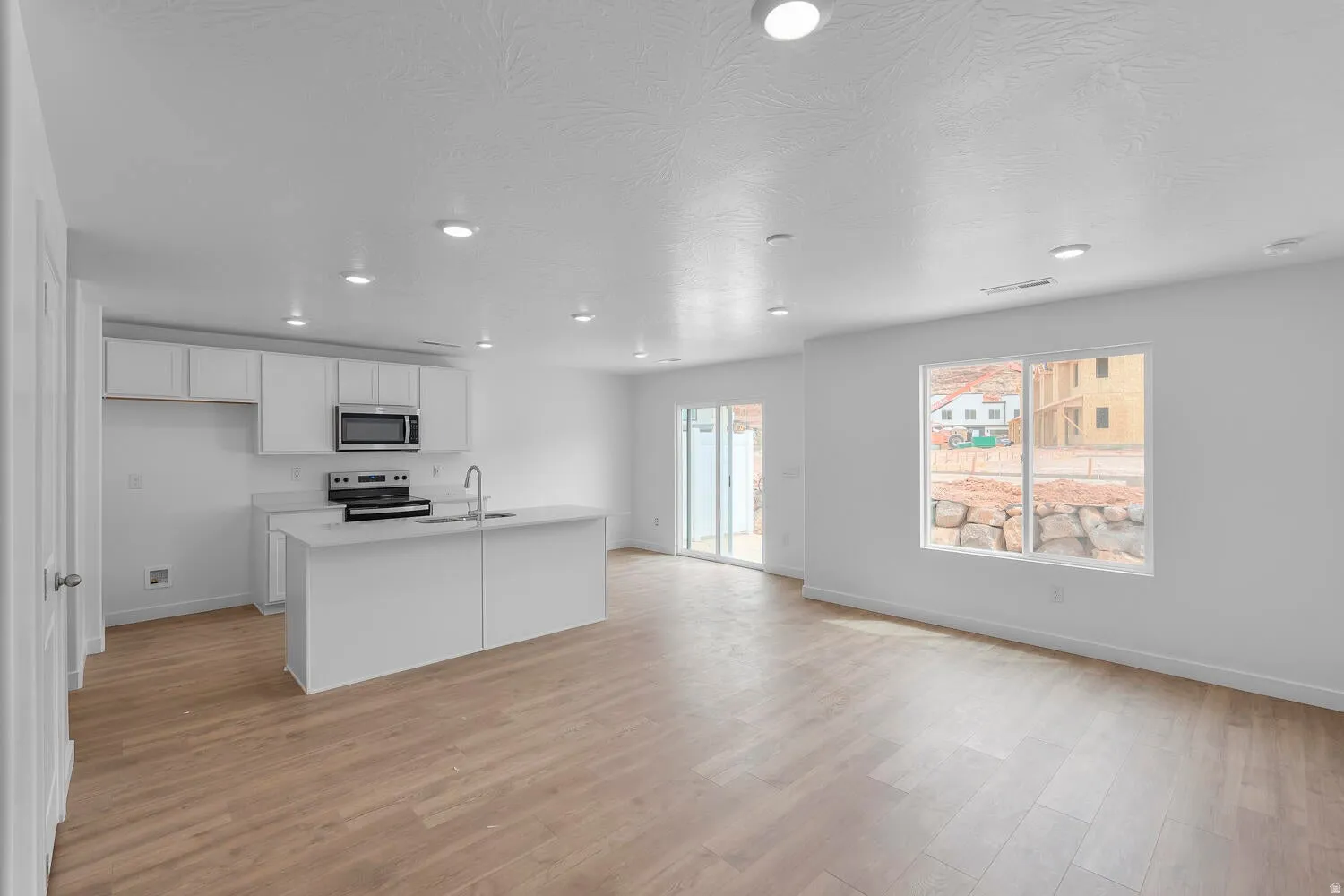 Kitchen featuring white cabinetry, a center island with sink, light wood finished floors, stainless steel appliances, and recessed lighting