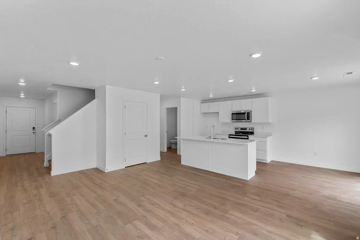 Kitchen with a kitchen island with sink, stainless steel appliances, light countertops, white cabinets, and open floor plan