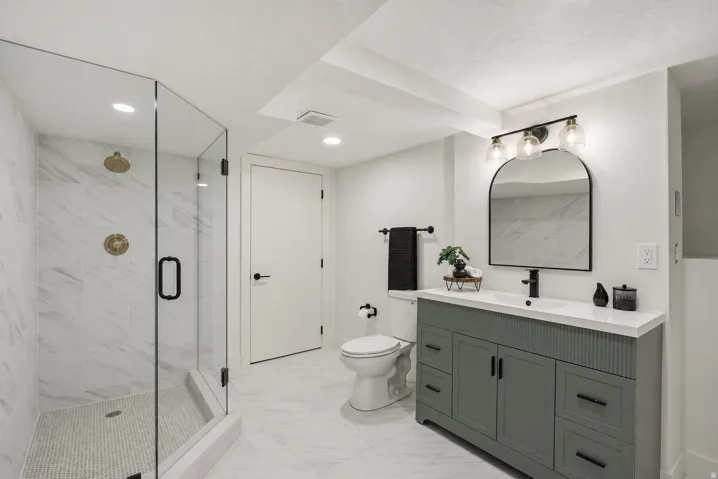 Modern bathroom featuring a glass-enclosed shower with gold-tone fixtures, a built-in shower niche, and white marble-look tile