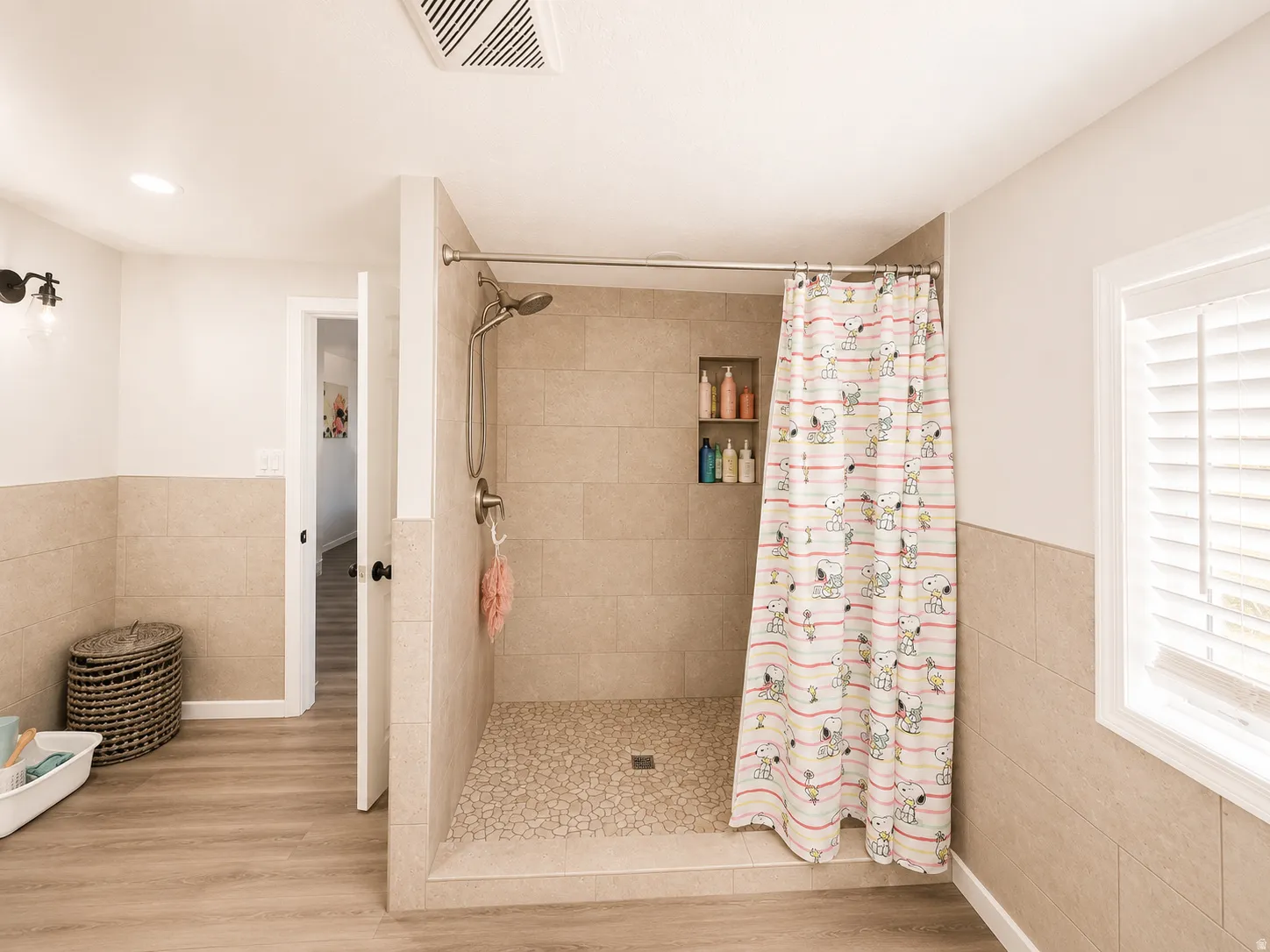 Walk-in shower featuring light-toned large format tile, pebble flooring, and built-in shelving