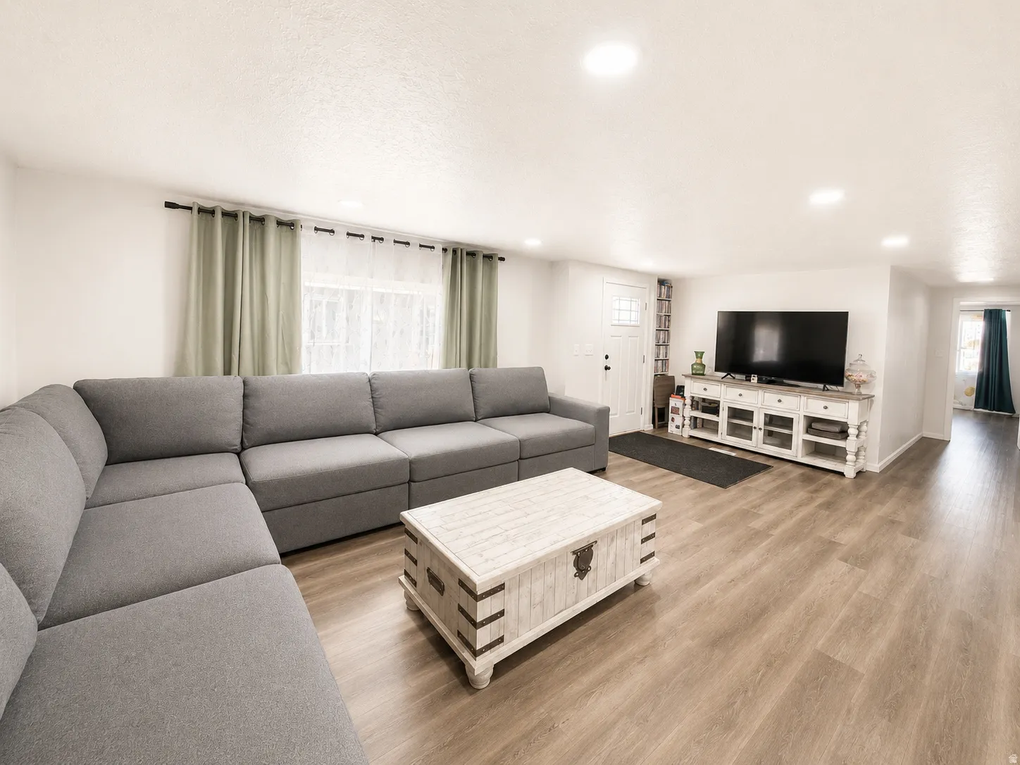 Spacious interior featuring light wood-finish flooring, recessed lighting, white walls, and a white paneled entry door