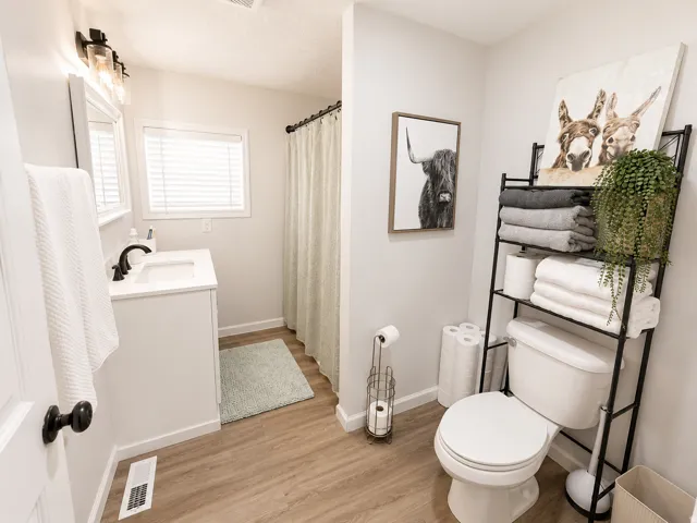 Bathroom featuring wood-finish flooring, a white vanity with a dark bronze faucet, and a window with blinds