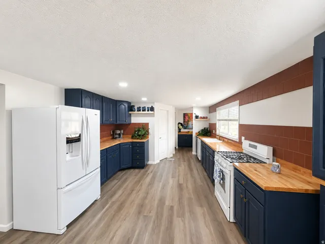 Spacious kitchen featuring wood-finish flooring, deep blue cabinetry, butcher block countertops, and a full-size refrigerator