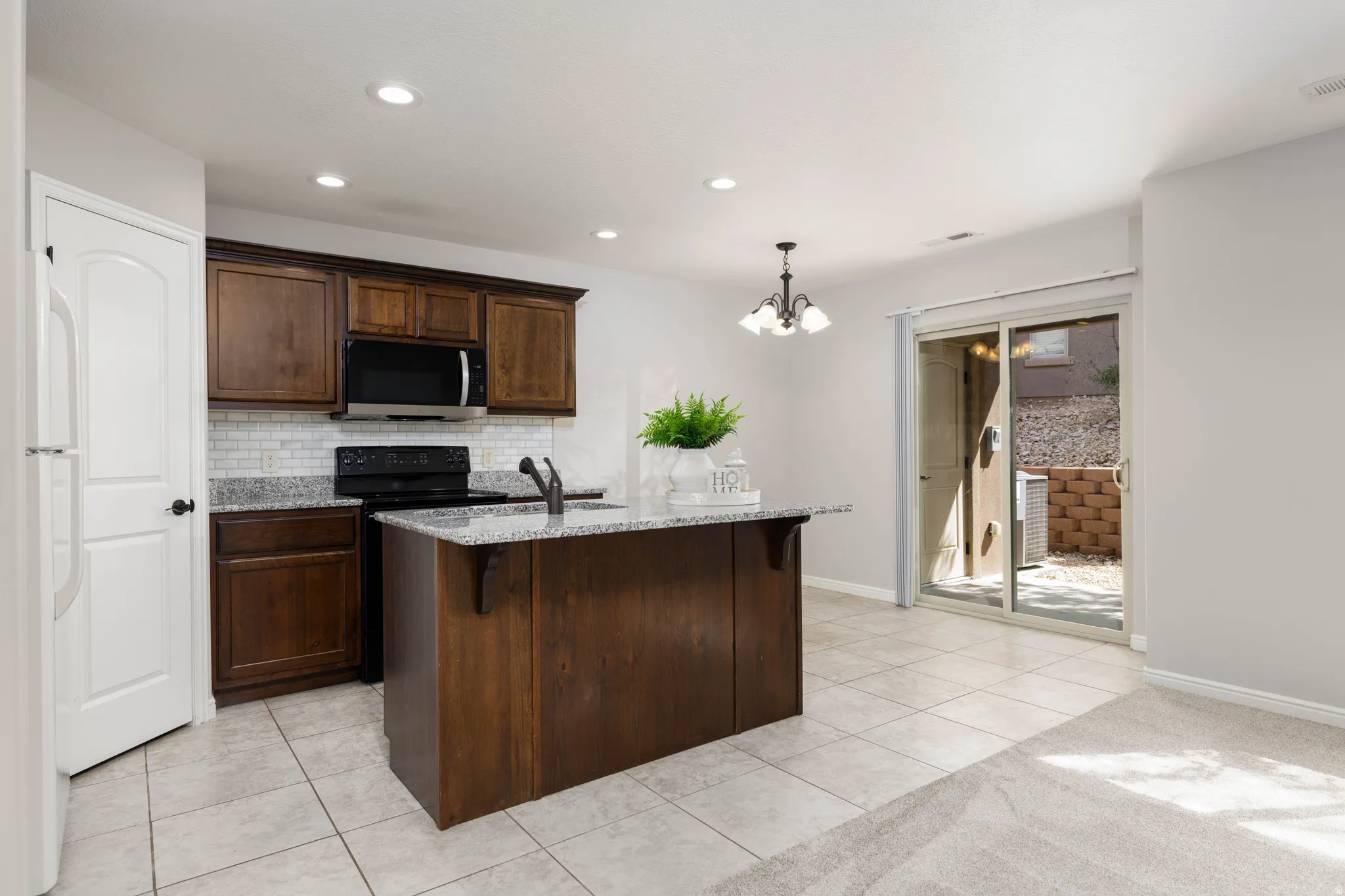 Kitchen with light tile flooring, granite counters, black range with electric stovetop, a kitchen breakfast bar, and a center island with sink