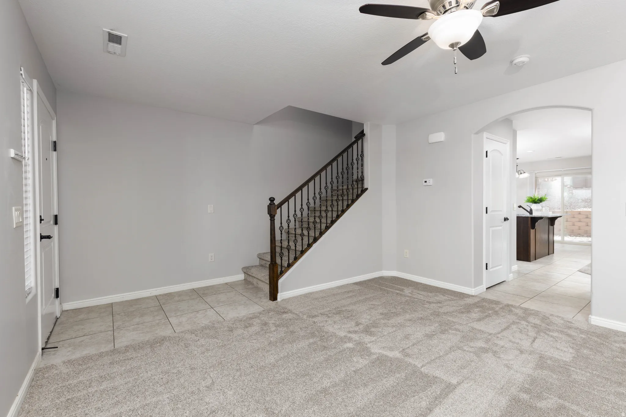 Entrance foyer with light tile, ceiling fan, arched walkways, and light carpet