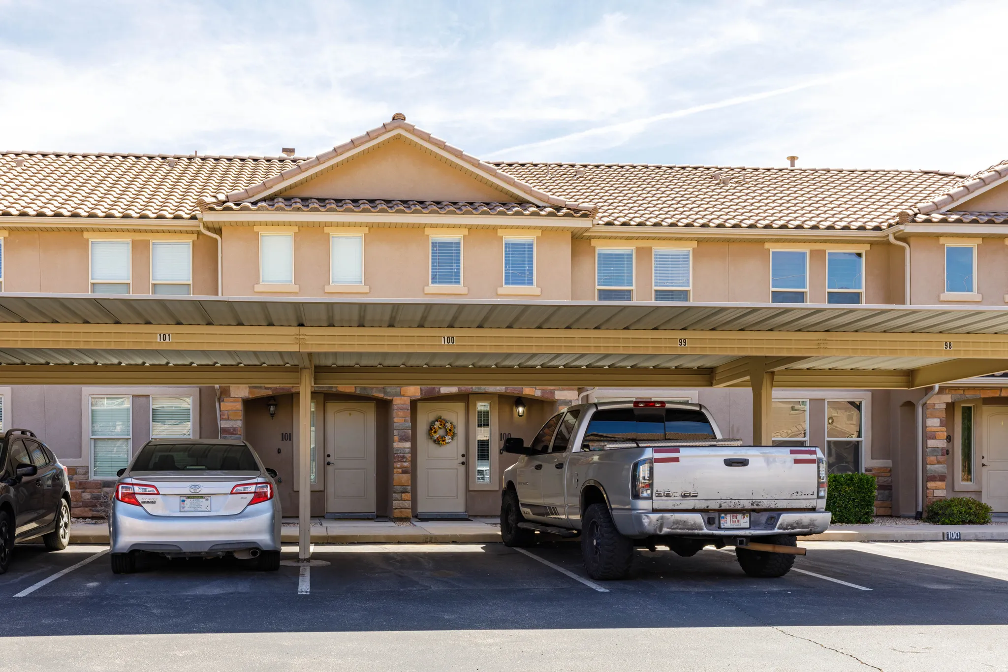 View of front of home featuring a tile roof, stucco siding, stone siding, and covered parking