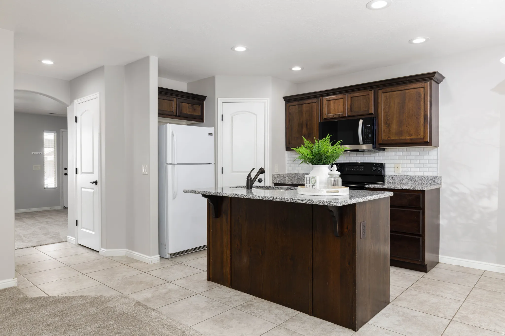 Kitchen with freestanding refrigerator, dark wood finish cabinetry, a kitchen breakfast bar, and granite counters