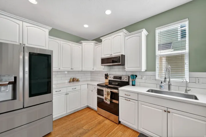 Kitchen featuring stainless steel appliances, white cabinetry, light wood finished floors, light stone countertops, and recessed lighting