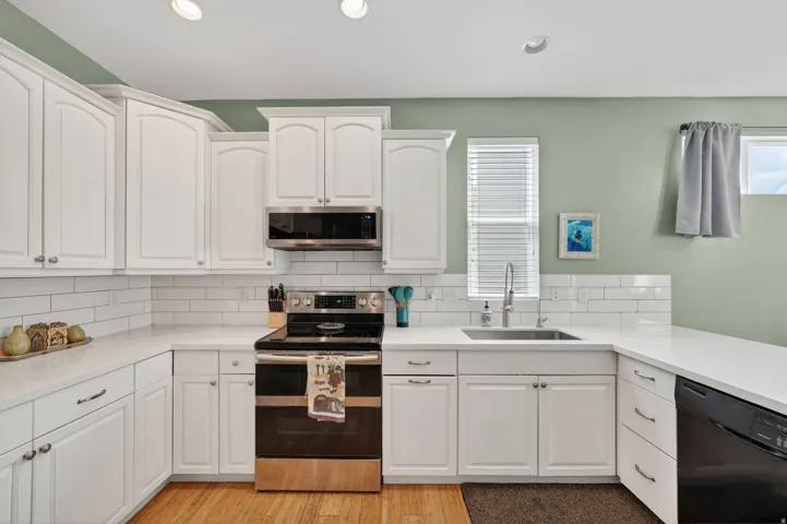 Kitchen with white cabinets, stainless steel appliances, light stone countertops, light wood-style flooring, and recessed lighting