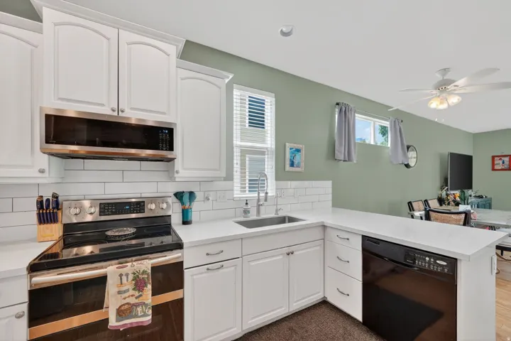 Kitchen with stainless steel appliances, white cabinets, a peninsula, backsplash, and ceiling fan